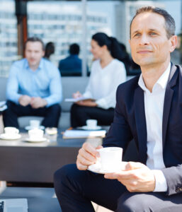 business man holding coffee cup looking into the distance while sitting at coffee shop outside